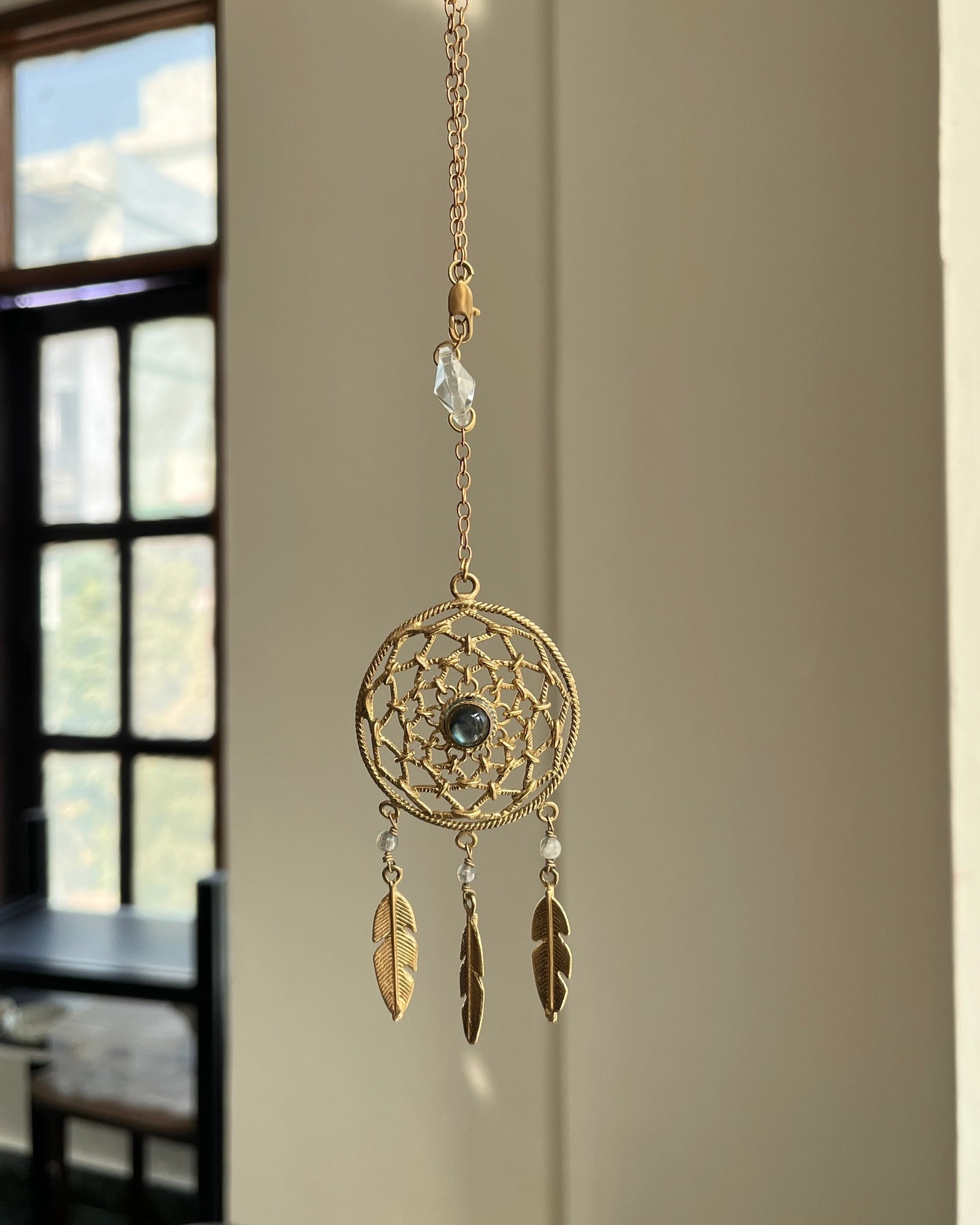 Brass dreamcatcher-shaped car charm with a central gemstone and feather hangings handmade by A Creator's Studio