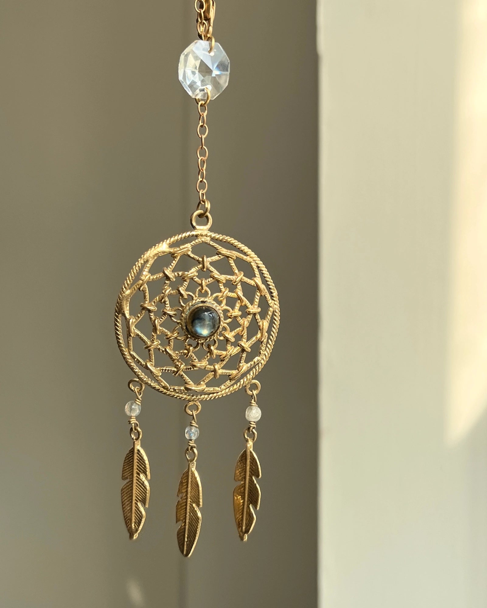 Brass dreamcatcher-shaped car charm with a central gemstone and feather hangings handmade by A Creator's Studio