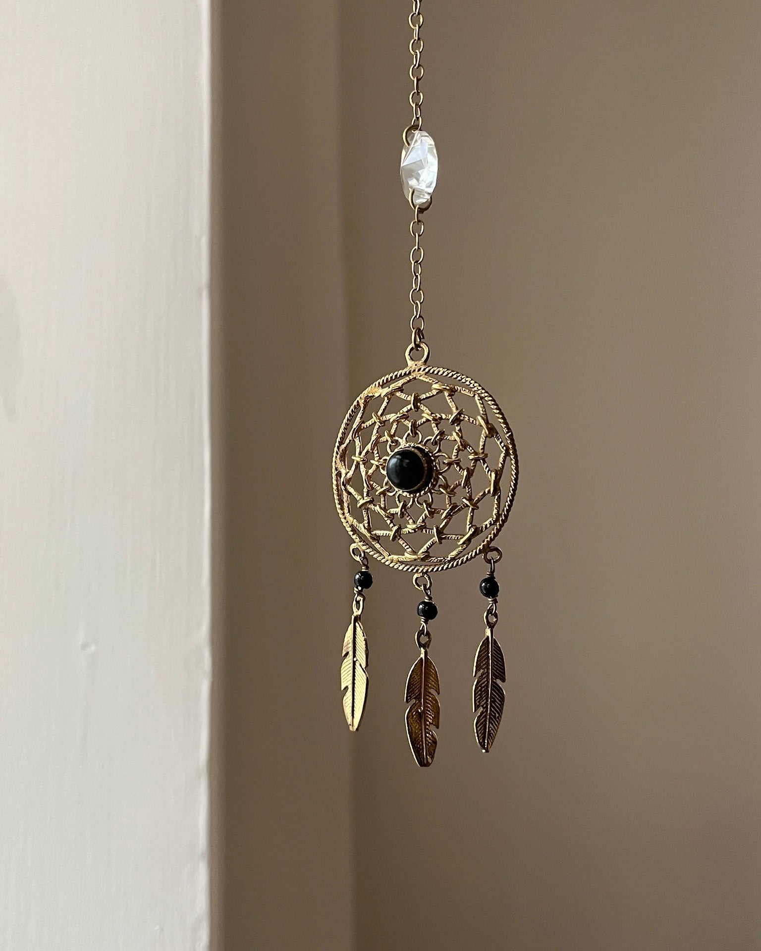 Brass dreamcatcher-shaped car charm with a central gemstone and feather hangings handmade by A Creator's Studio