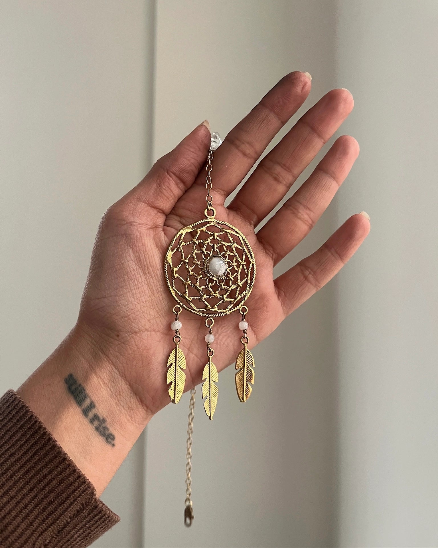 Brass dreamcatcher-shaped car charm with a central gemstone and feather hangings handmade by A Creator's Studio