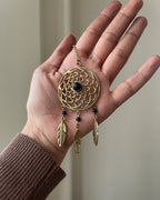 Brass dreamcatcher-shaped car charm with a central gemstone and feather hangings handmade by A Creator's Studio
