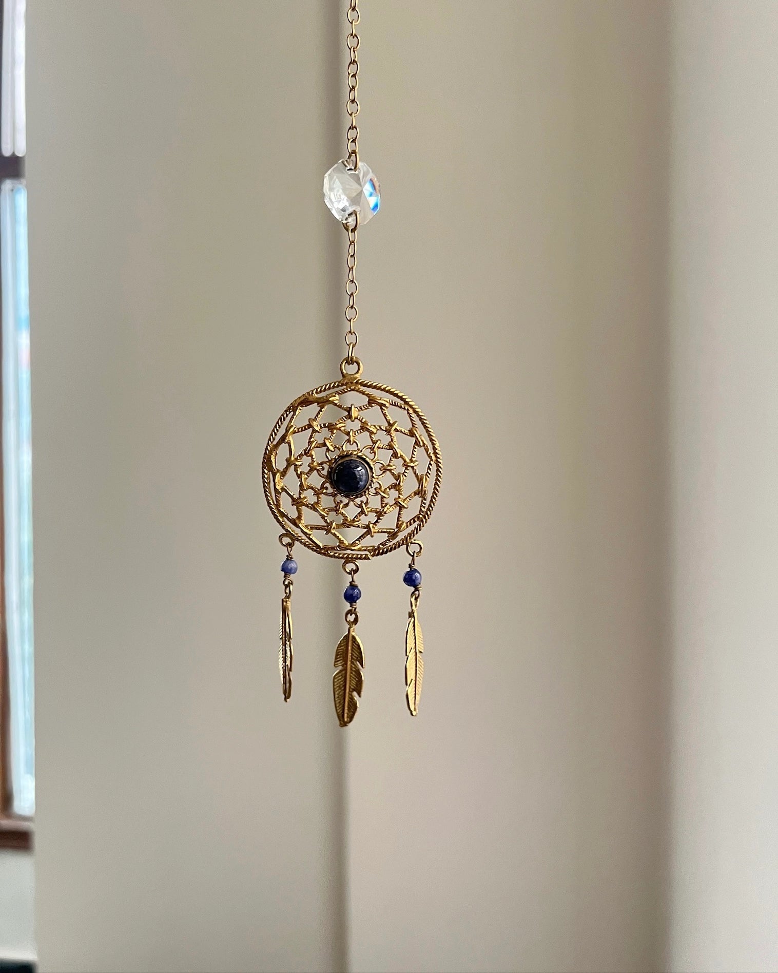 Brass dreamcatcher-shaped car charm with a central gemstone and feather hangings handmade by A Creator's Studio