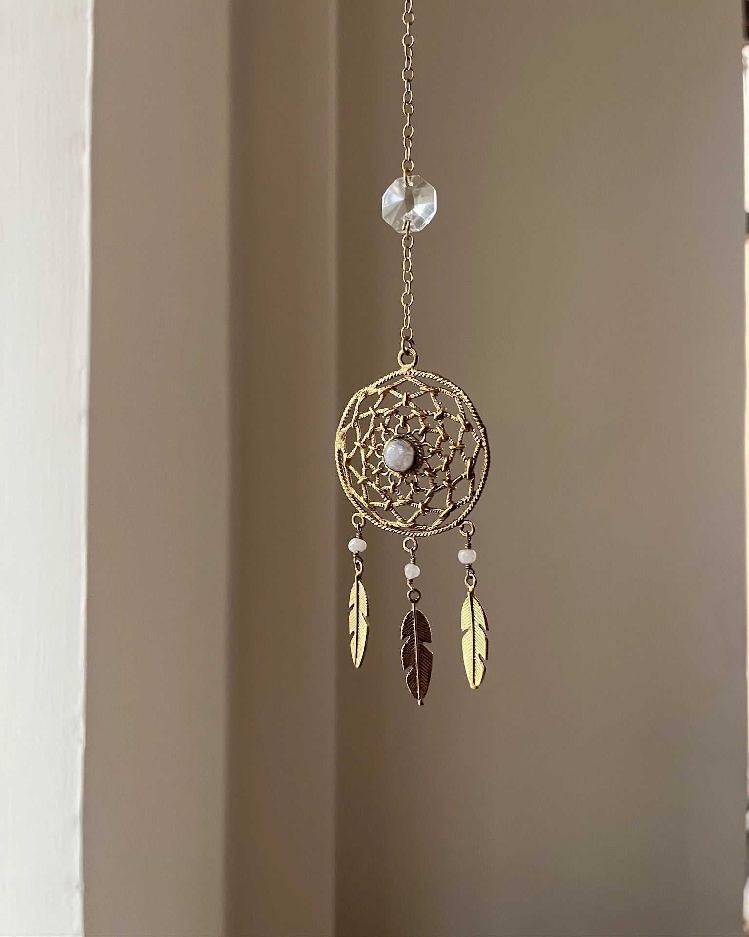 Brass dreamcatcher-shaped car charm with a central gemstone and feather hangings handmade by A Creator's Studio