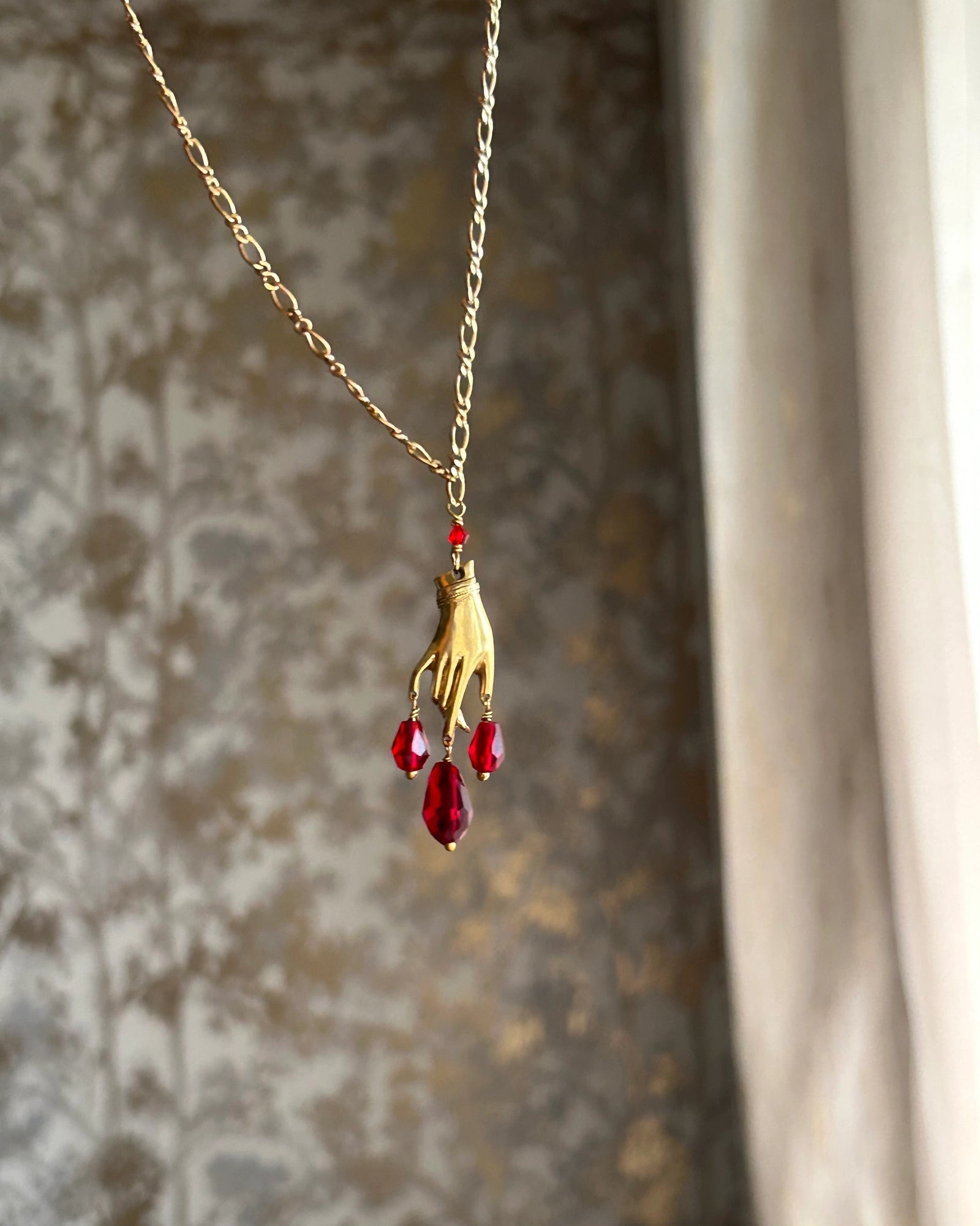 Brass necklace with a hand pendant and red crystal drops handmade by A Creator's Studio